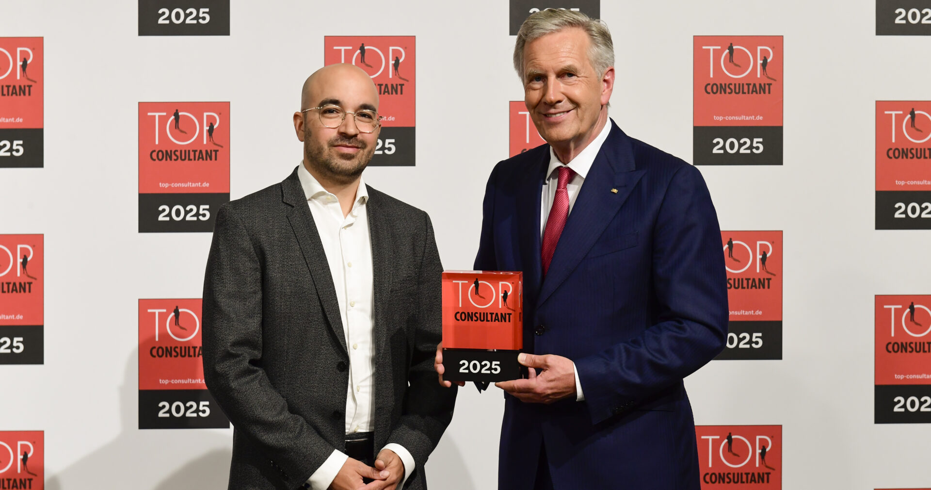 Zwei Männer halten Top Consultant Trophäe 2025.