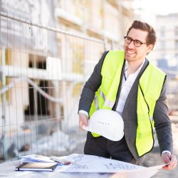 Freudig lächelnder Architekt auf der Baustelle mit Bauplänen